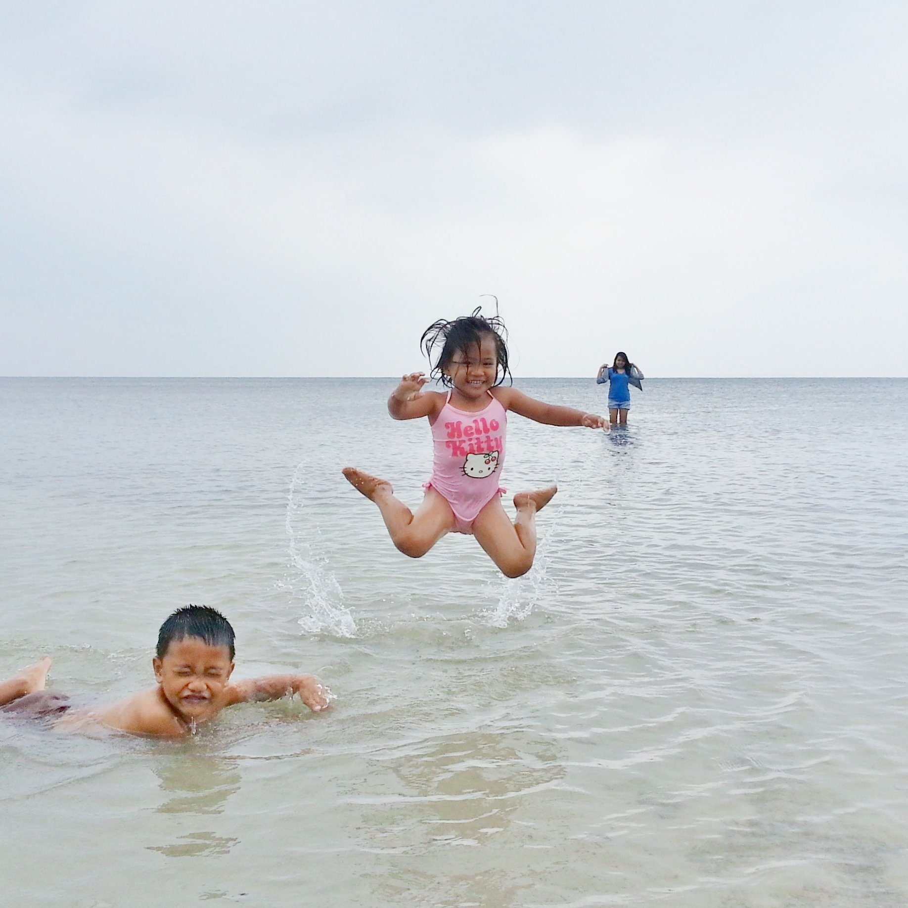 Criança pulando na água da praia sorrindo