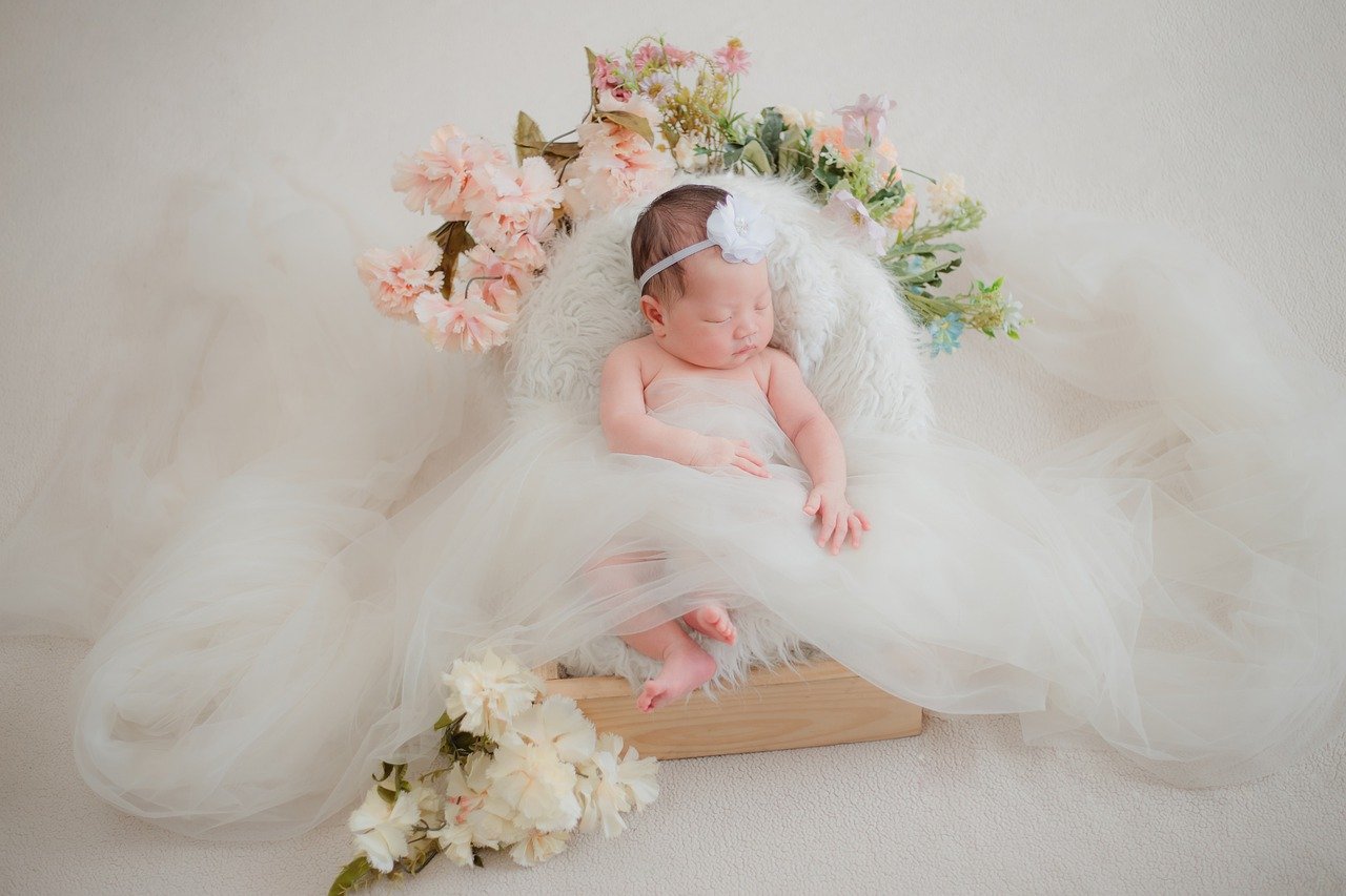 Bebê em cadeirinha decorada com flores, folhas e tecidos brancos