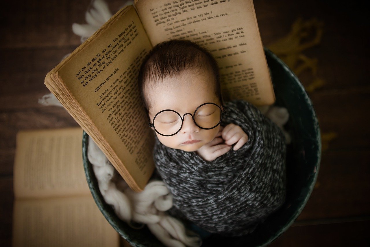 Bebê de óculos estilo nerd dentro de cesto com livro antigo