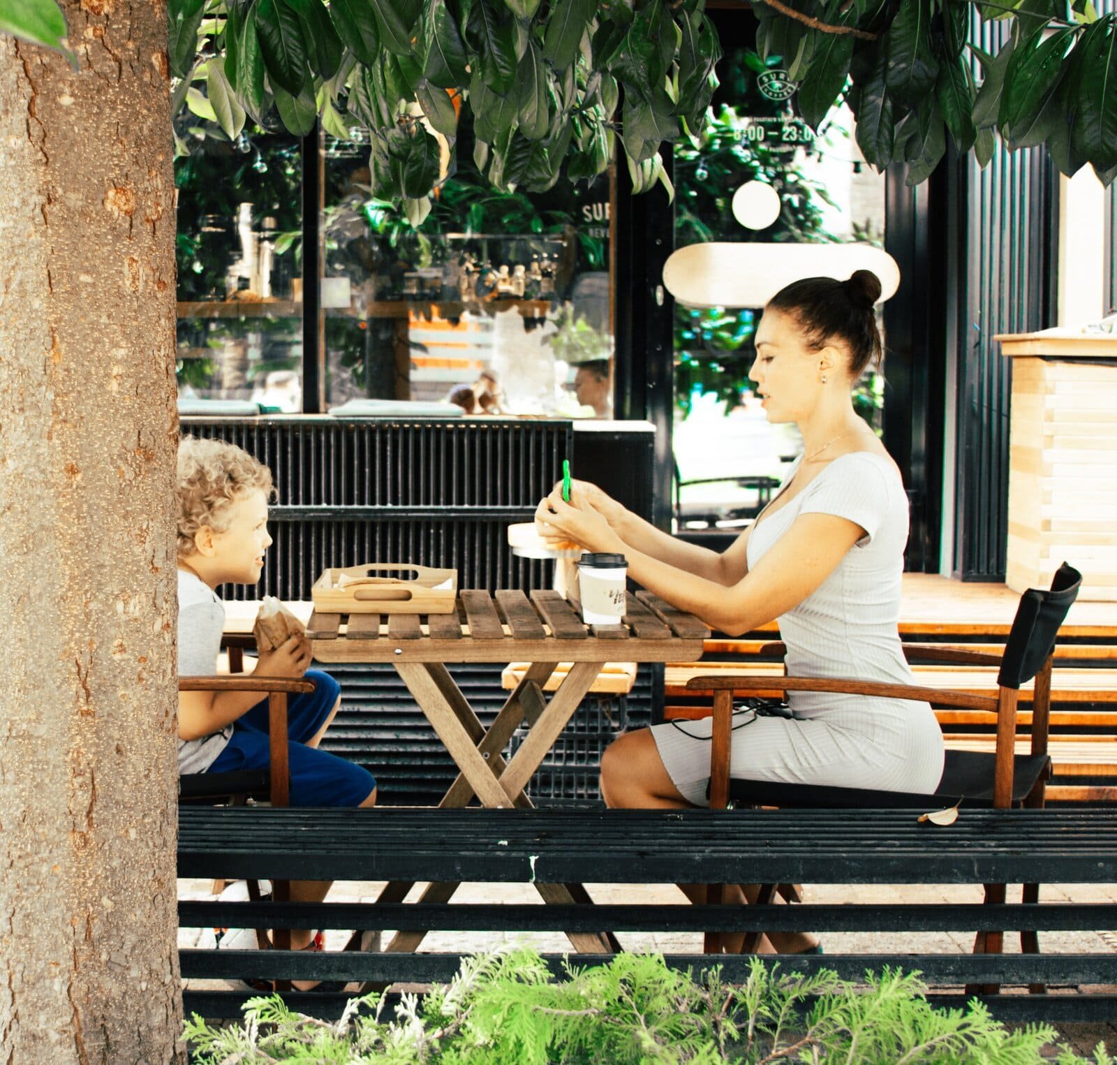 Mulher e uma criança sentados em uma mesa de madeira tomando café.