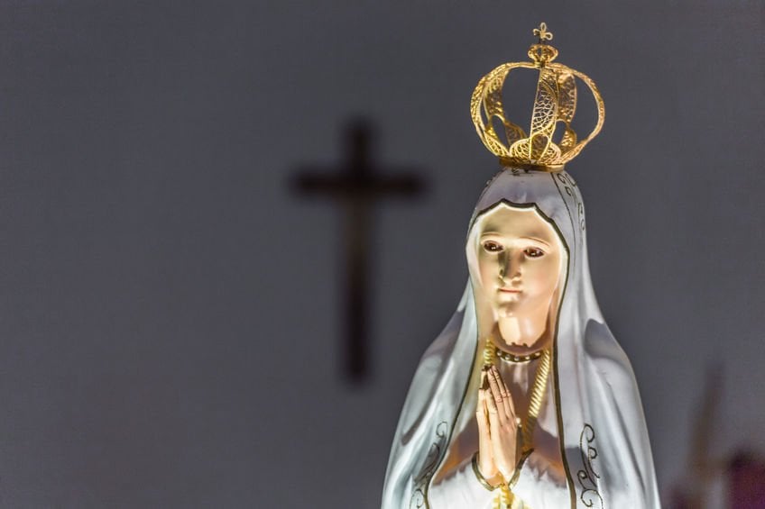Estátua de Nossa Senhora com as palmas unidas em frente ao peito.