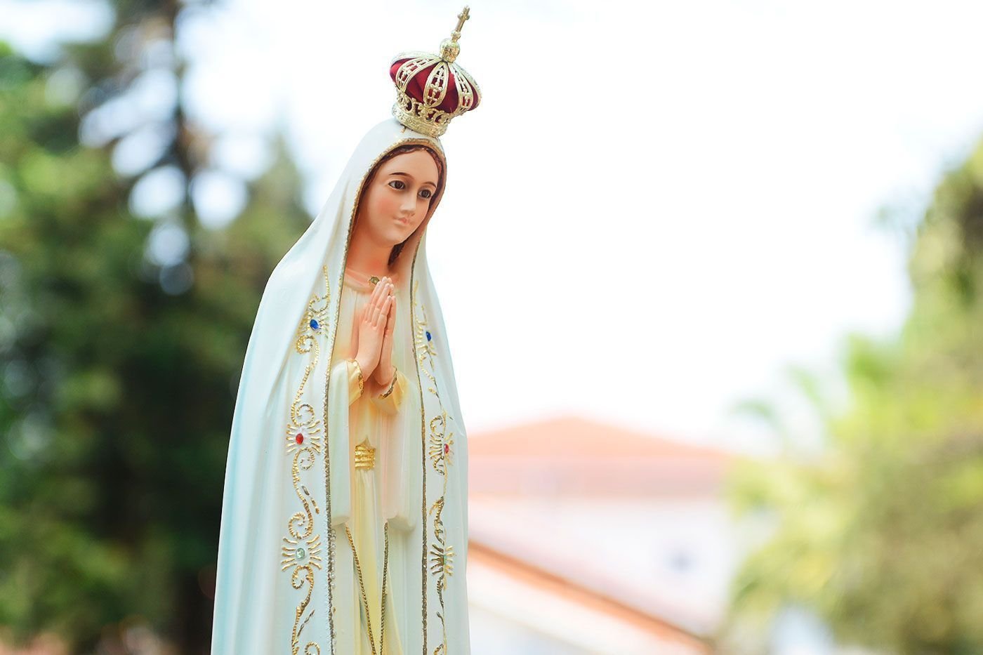 Estátua da Nossa Senhora com coroa e as palmas unidas em frente ao seu corpo.
