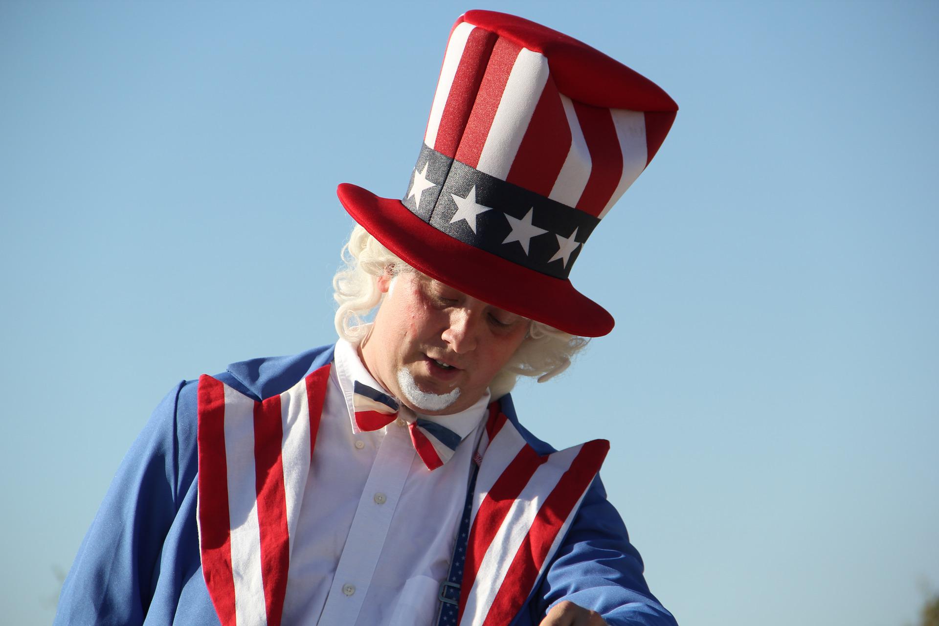Homem vestindo uma cartola e um paletó com as cores da bandeira norte-americana. Veste uma barba e uma peruca branca