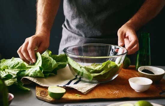 Homem cozinhando na cozinha, segurando um recipiente com salada