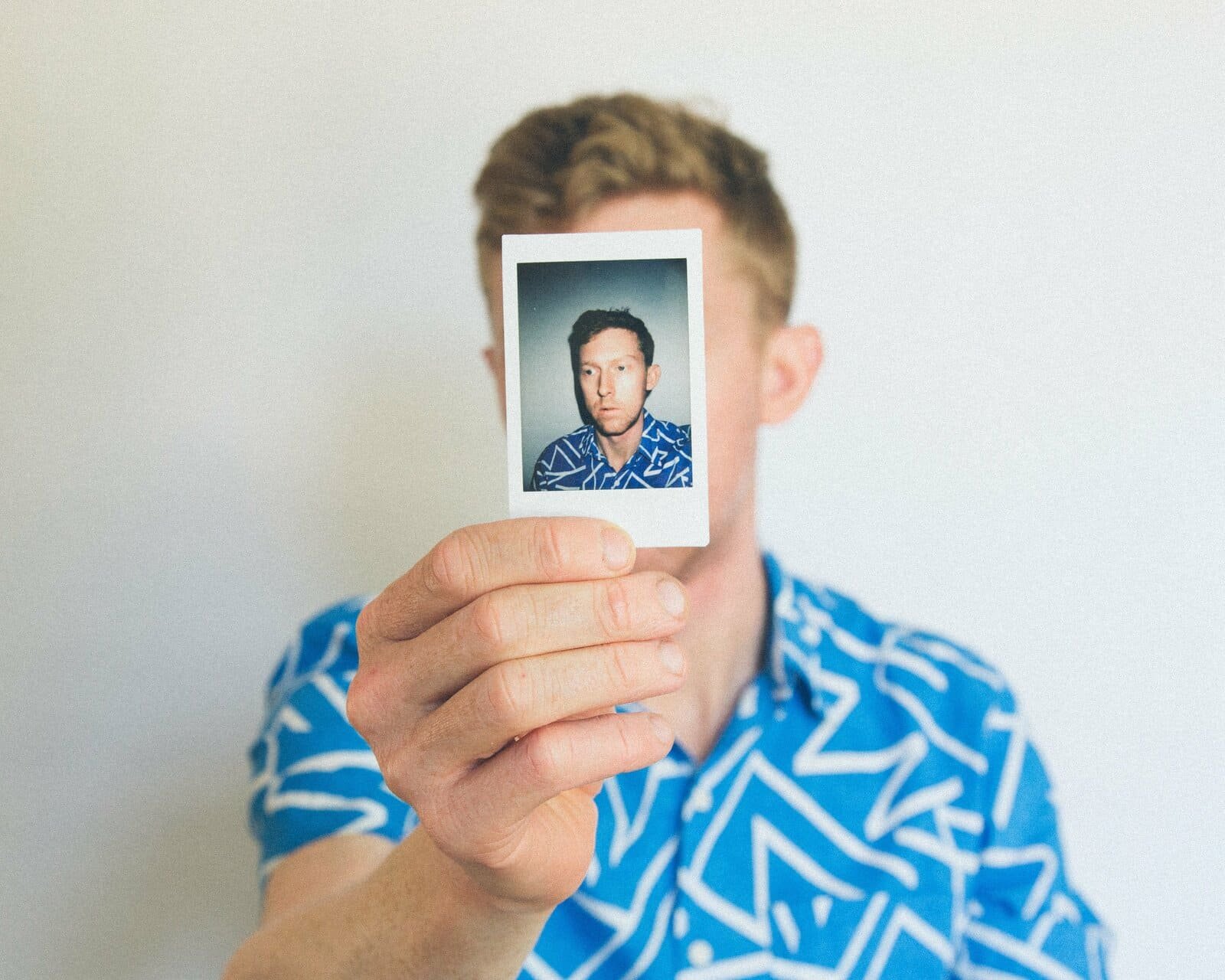 Homem segurando uma foto 3x4 de perfil em formato polaroid em frente ao rosto