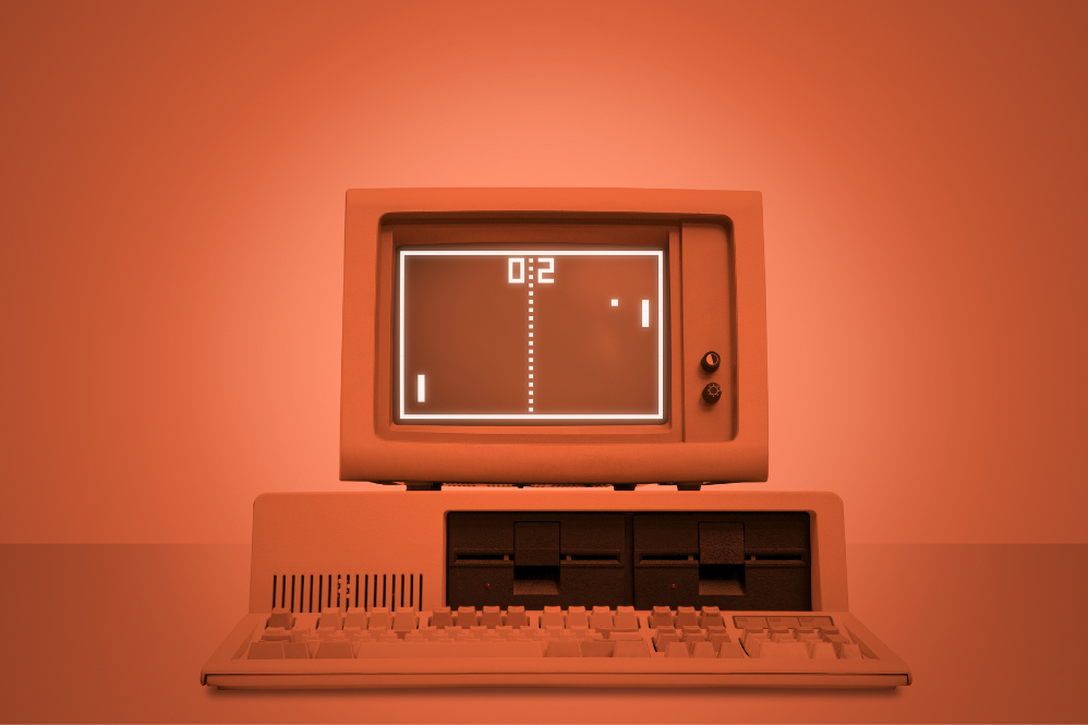 Um computador dos anos 80. Na tela, há um jogo pixelado, marcando 0 a 2.