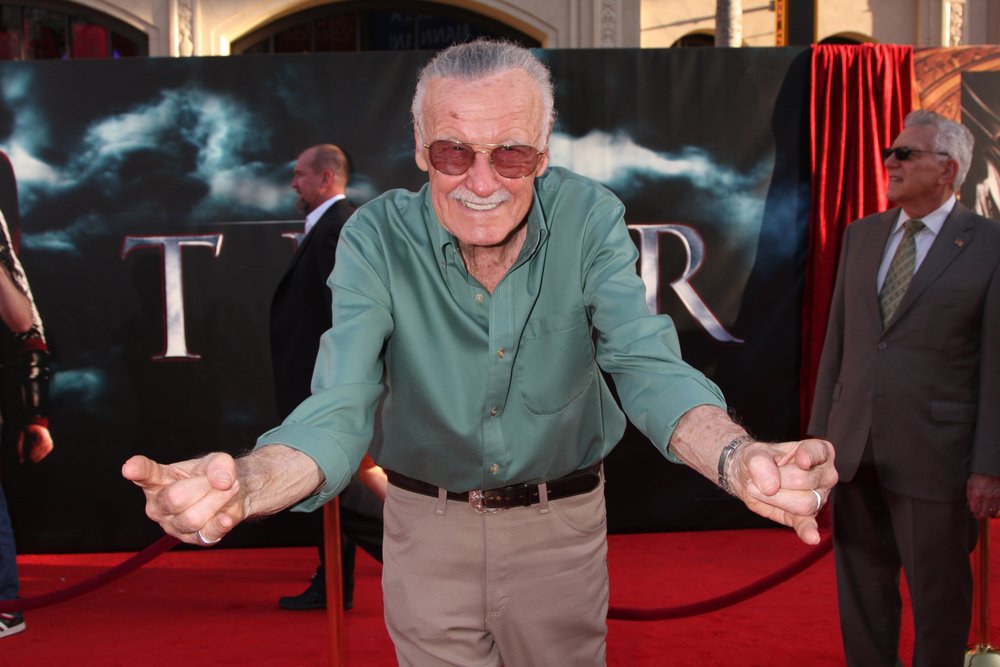 Stan Lee rindo e fazendo sinal do Homem Aranha com as duas mãos