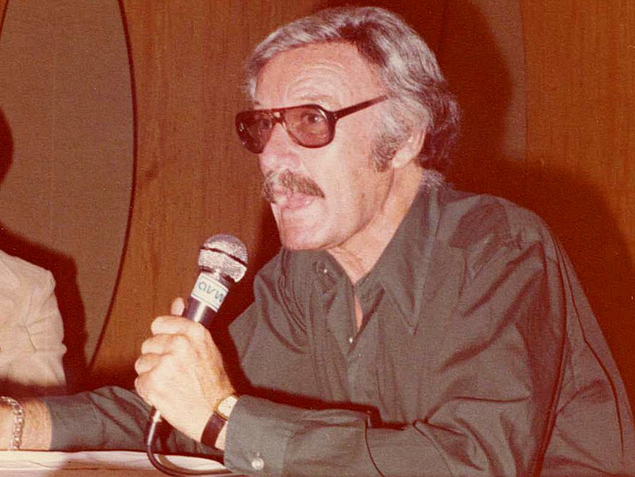 Stan Lee jovem, nos anos 80, palestrando com microfone