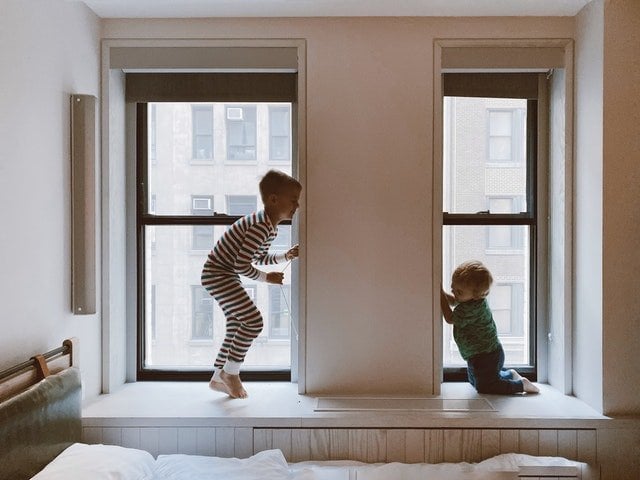 Dois meninos brancos de pijamas brincando próximo à janela