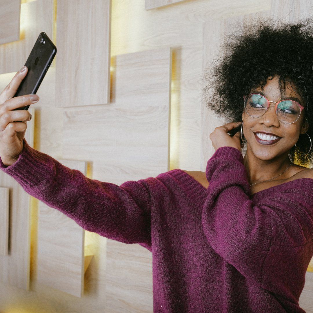 Mulher de óculos sorrindo e tirando uma selfie