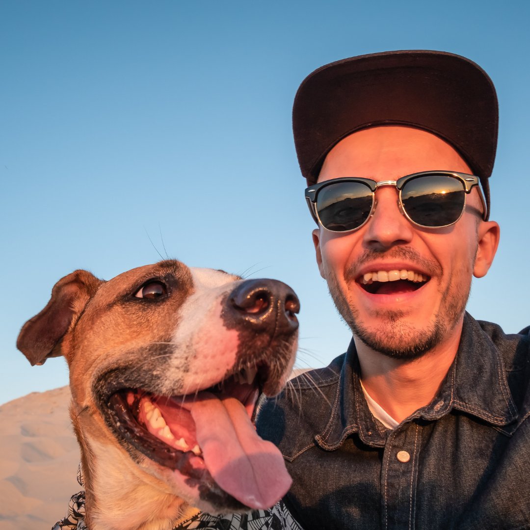 Homem com óculos de sol sorrindo e tirando foto com um cachorro