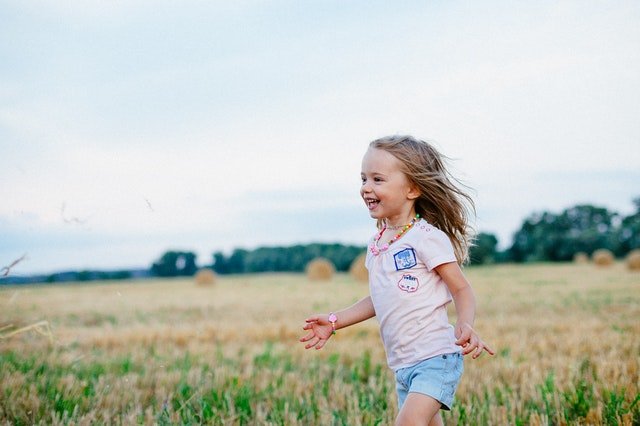 Menina sorri enquanto corre por um campo