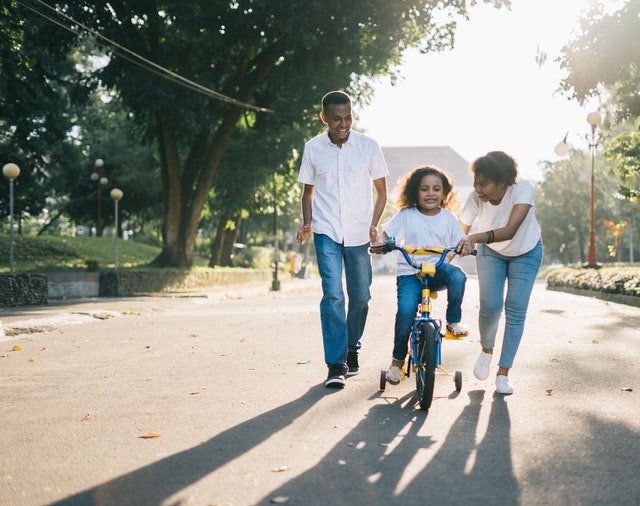 Mãe e pai ensinando sua filha a andar de bicicleta