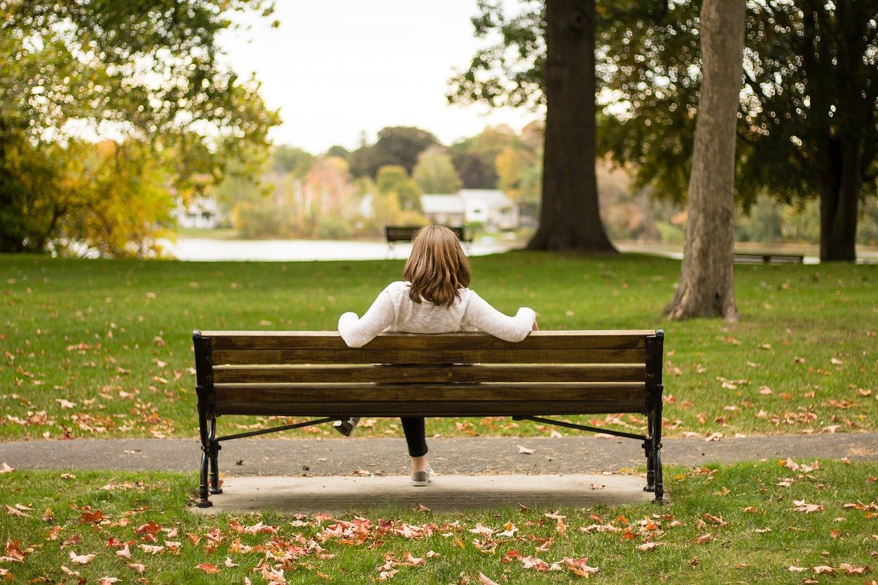 Mulher sentada em banco de praça sozinha, contemplando a vista