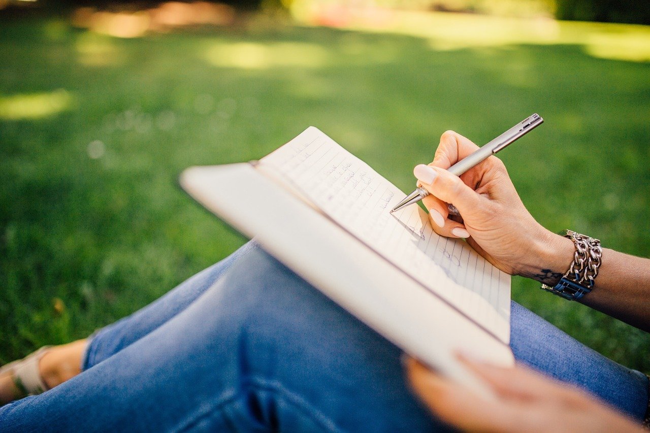 Mão feminina fazendo anotações em livro sobre campo gramado