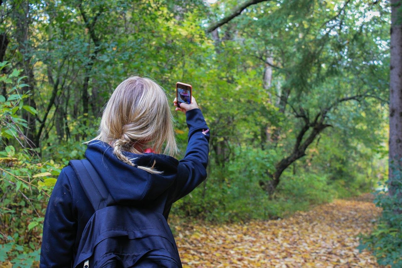 Mulher loira de costas tirando uma selfie no meio do mato