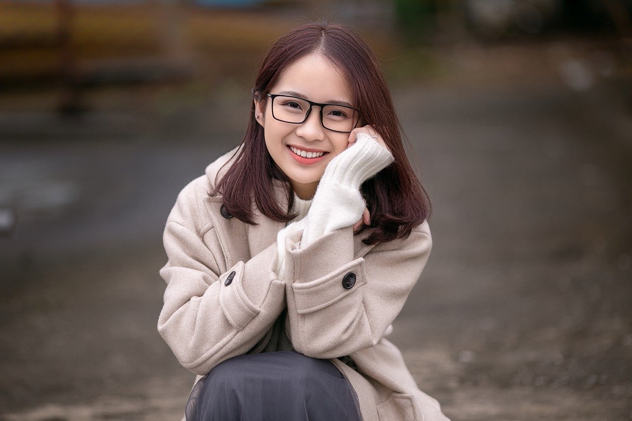 Mulher asiática de óculos com a mão no rosto sorrindo para foto