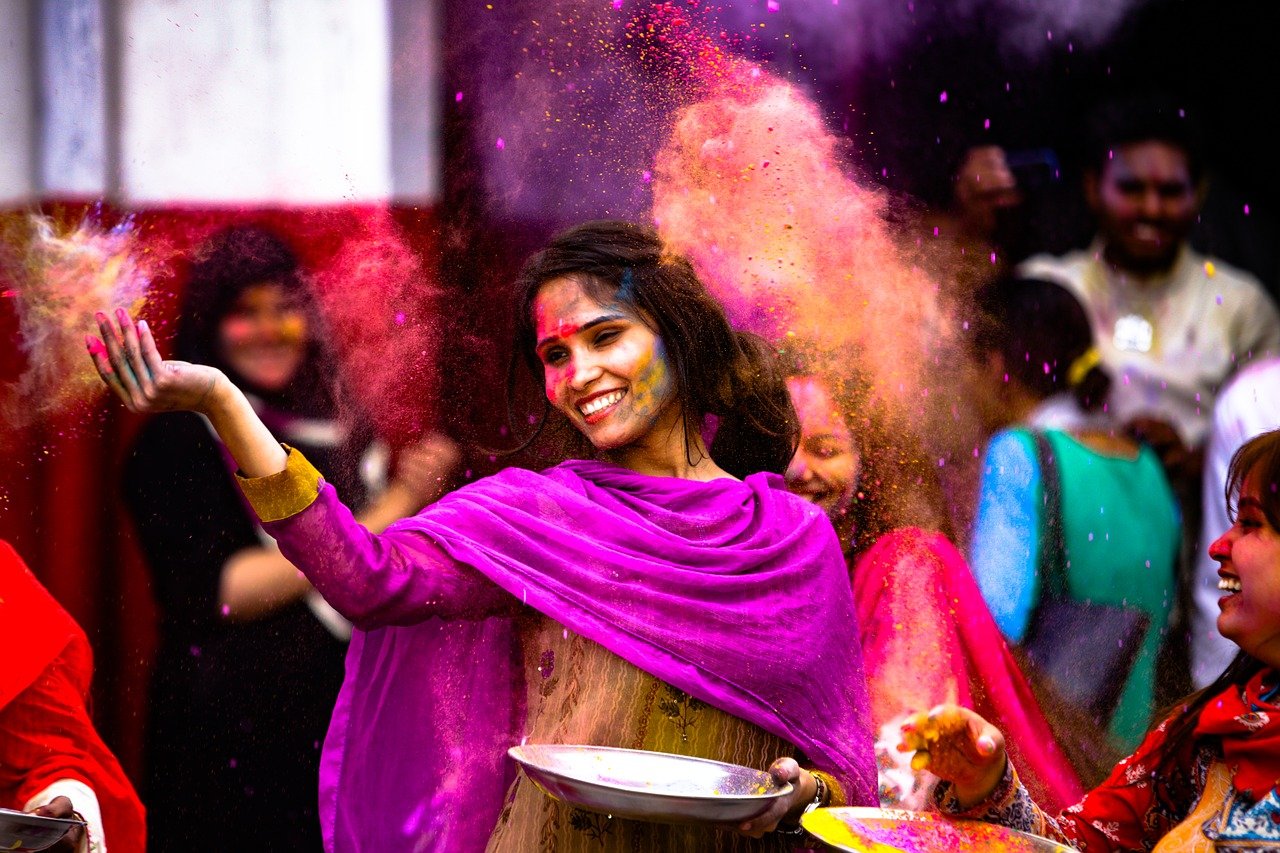 Mulher com trajes típicos indianos celebrando com pós coloridos no ar