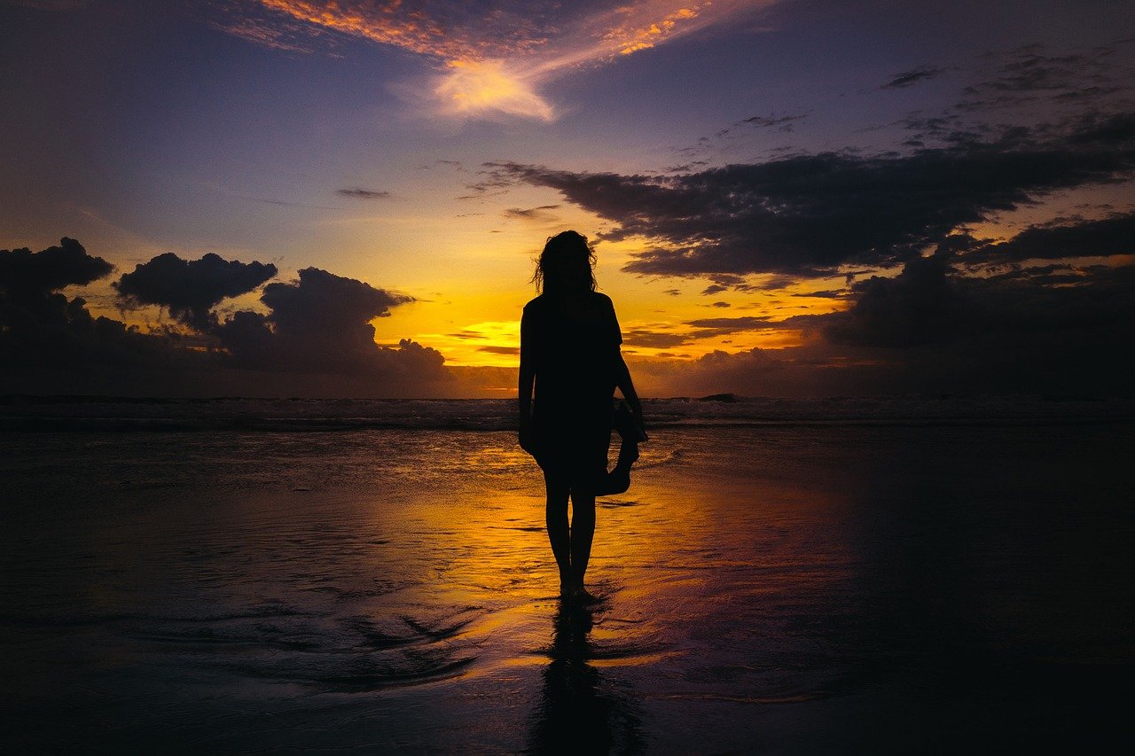 Silhueta de mulher na praia em meio ao por do sol