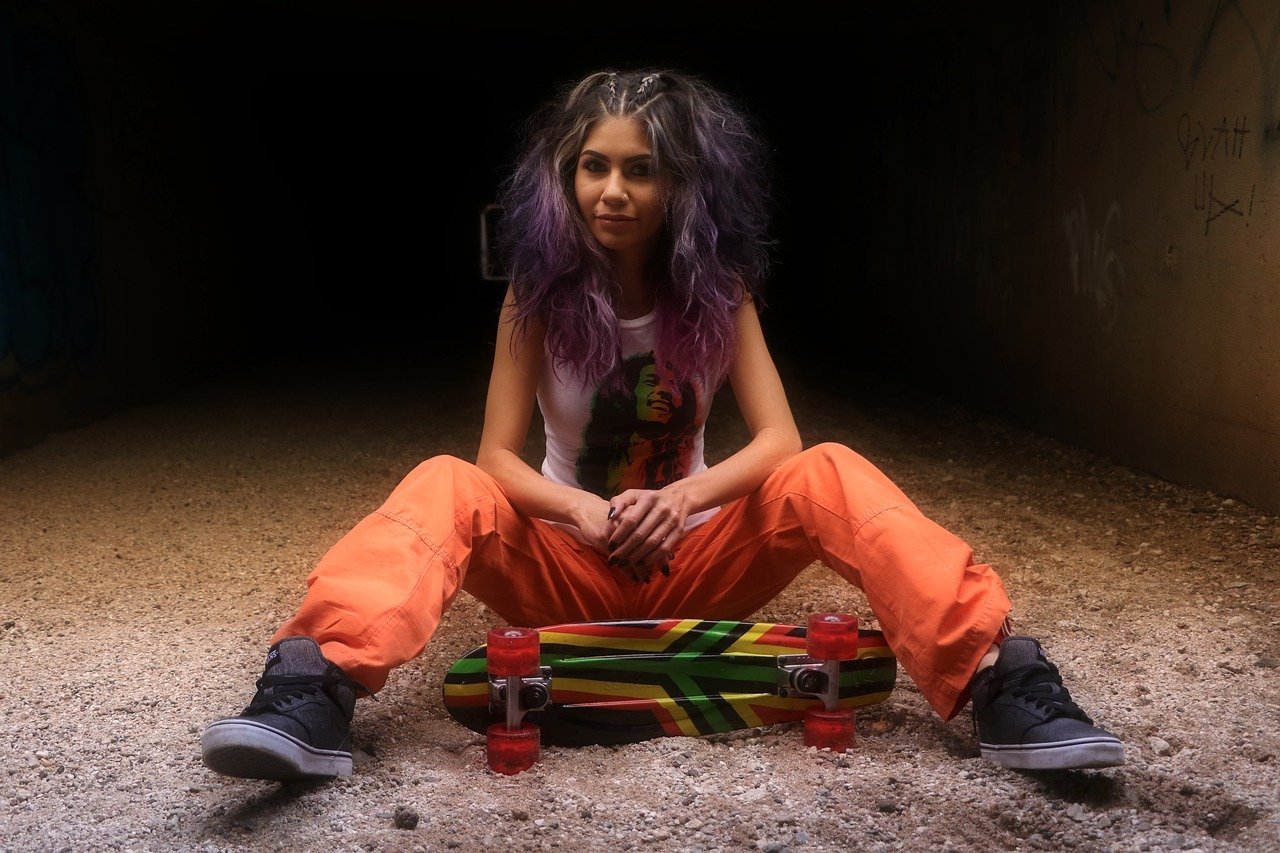 Mulher de cabelo roxo posando com seu skateboard