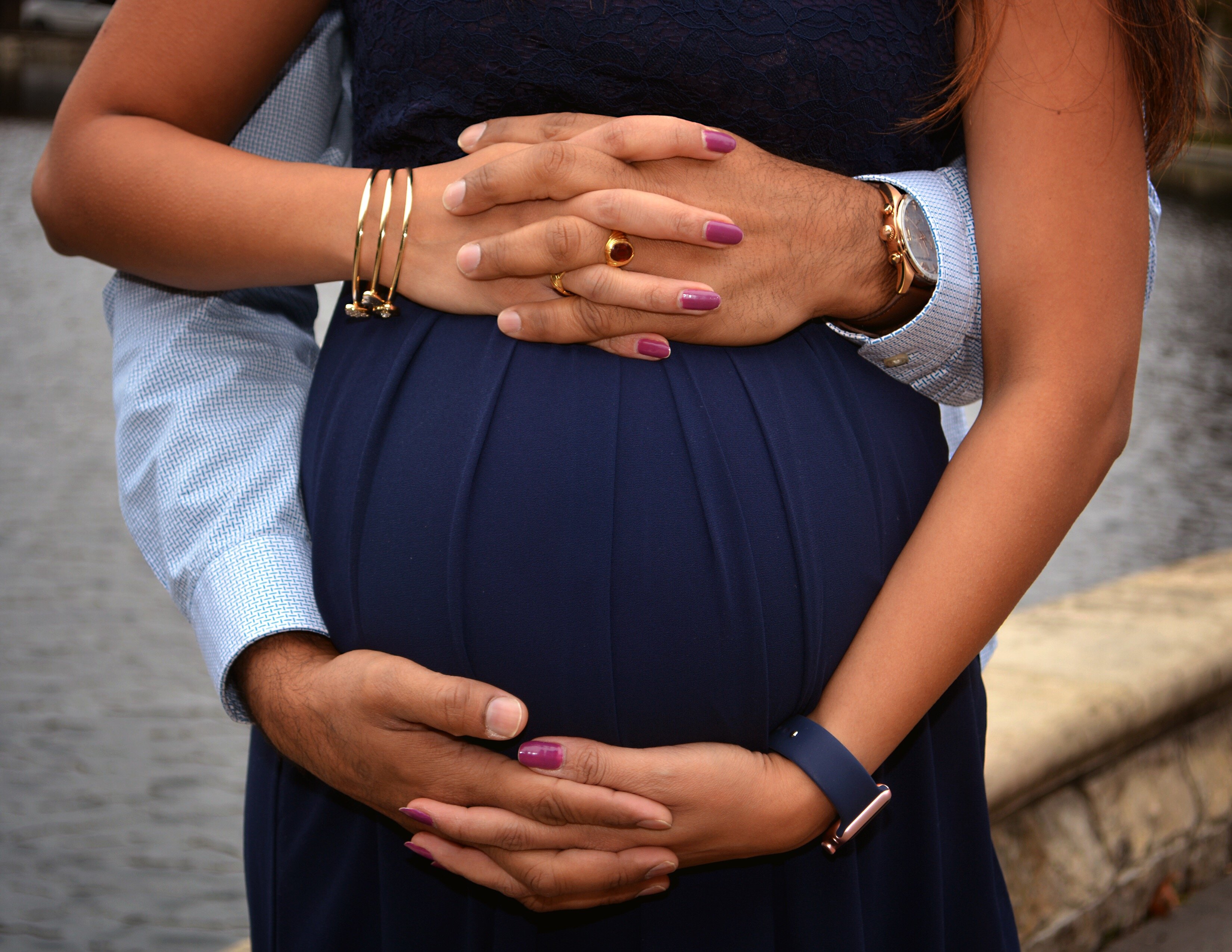 Mulher grávida segurando mãos de pessoa que está a abraçando por trás