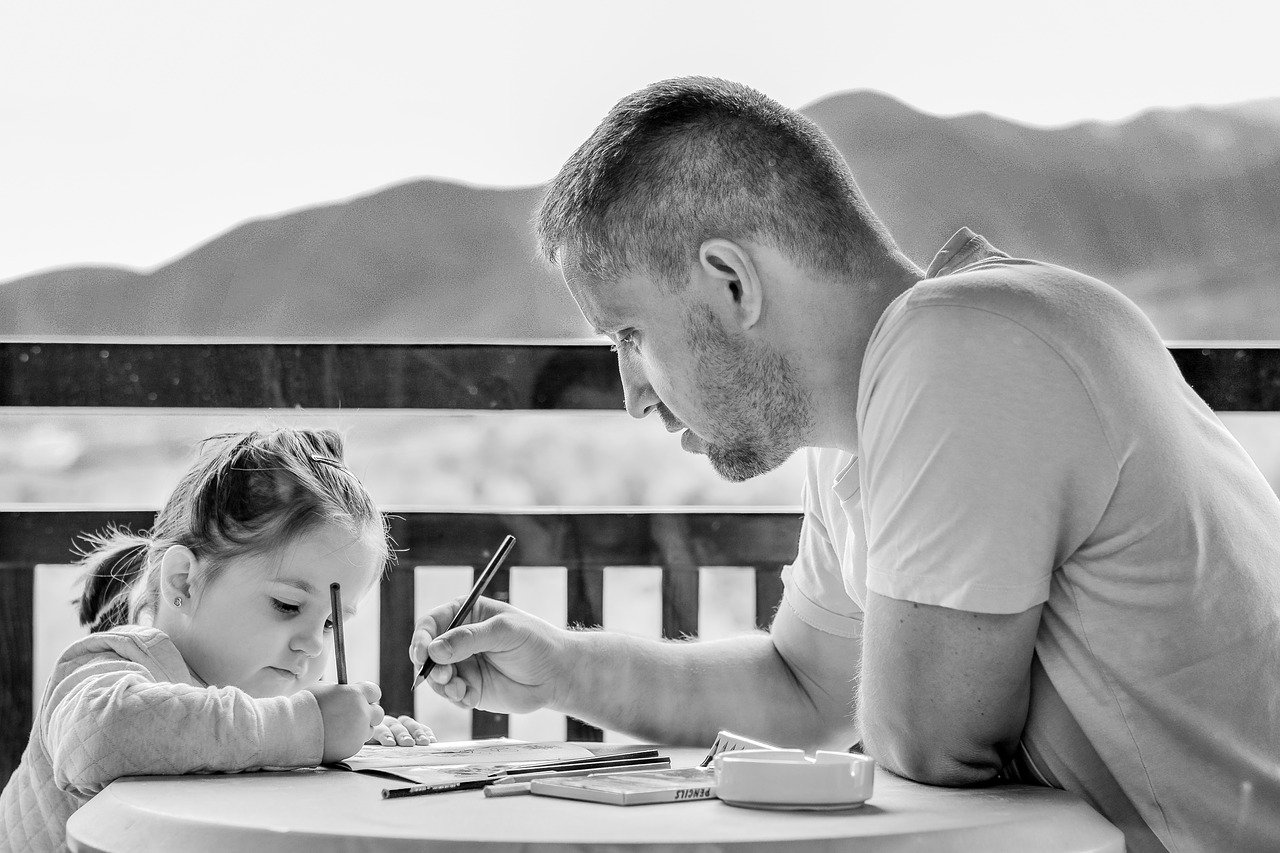 Homem desenhando em uma mesa com uma criança em sua frente
