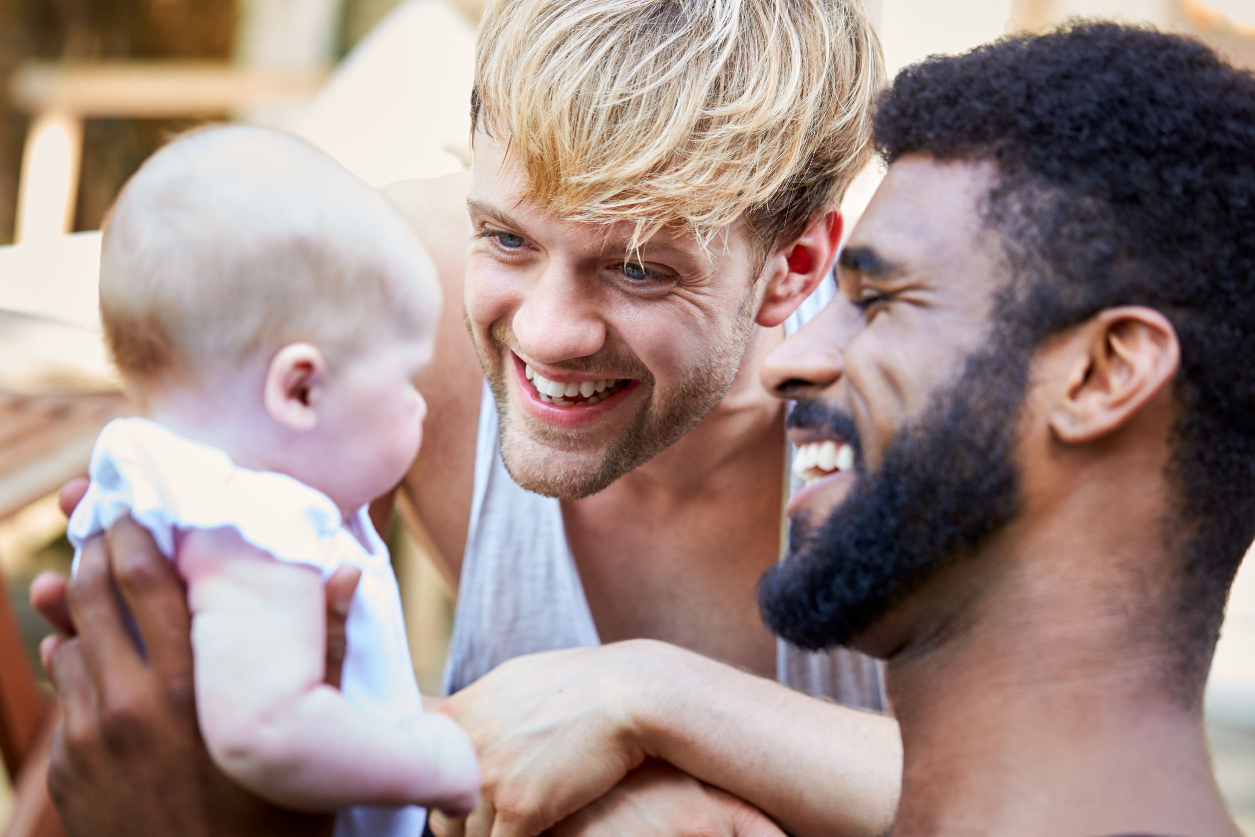 Dois homens segurando um bebê e sorrindo