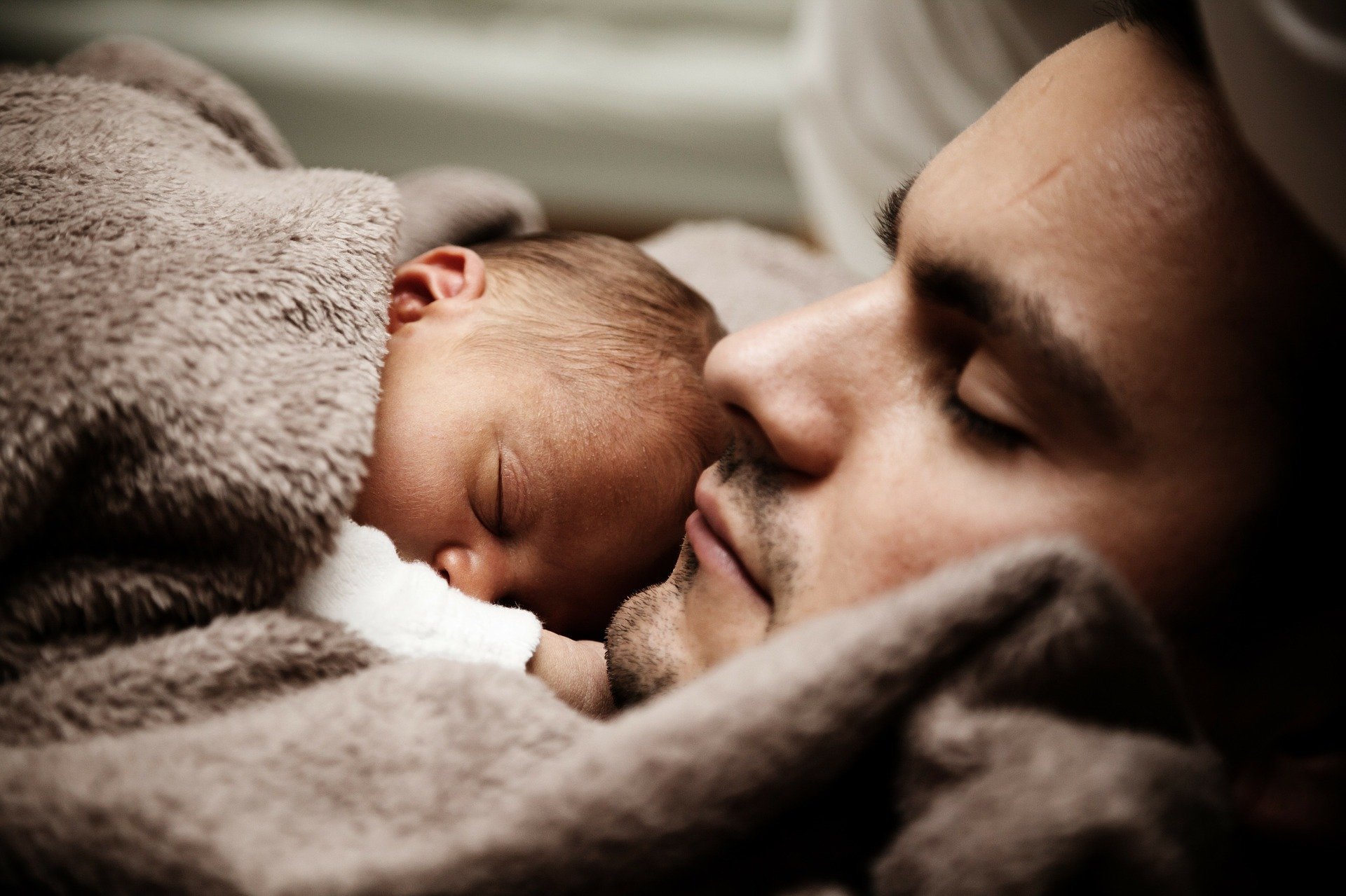 Homem de olhos fechados com bebê dormindo ao seu lado