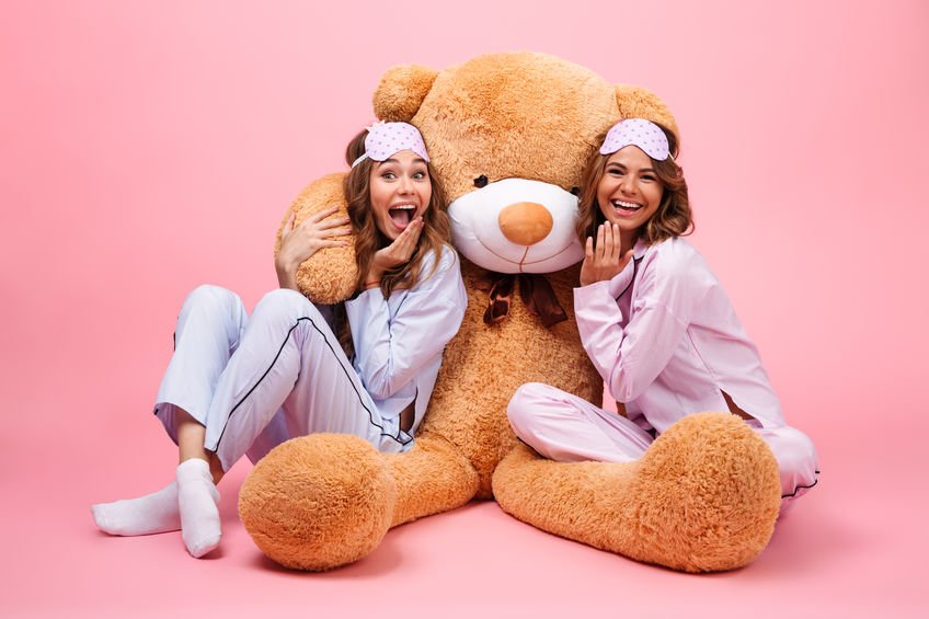 Irmãs de pijama abraçadas com urso de pelúcia gigante