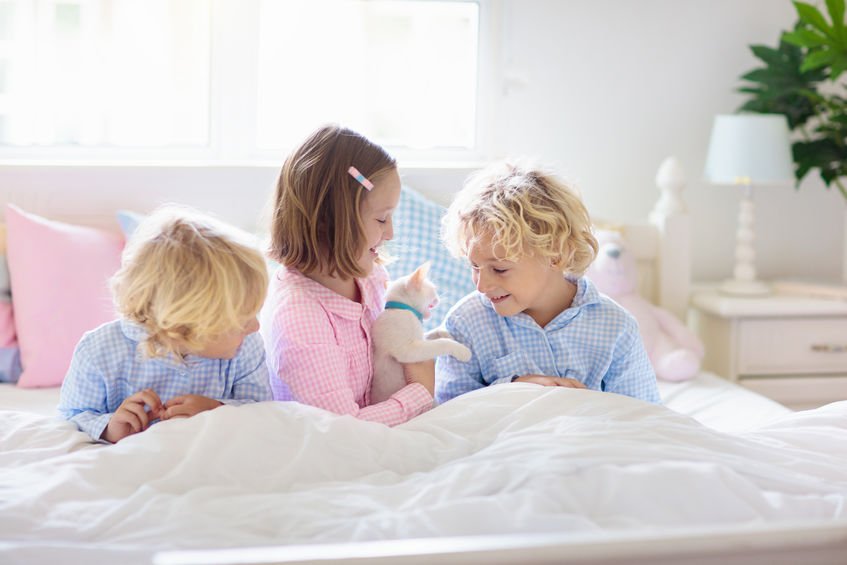 Três crianças (uma menina e dois meninos) deitadas em cama branca