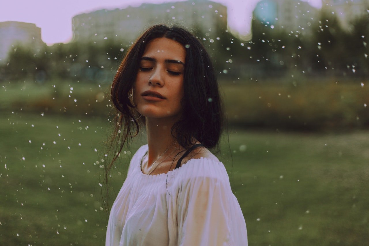 Mulher de olhos fechados num gramado, na chuva