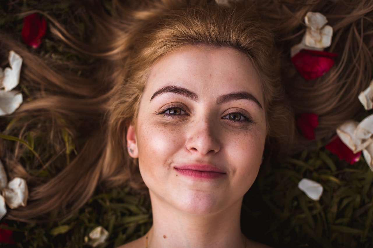 Mulher deitada, sorrindo, com pétalas de flor nos cabelos