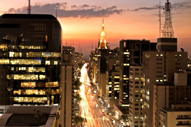 Avenida Paulista a noite. Há prédios com luzes ligadas e tudo está iluminado