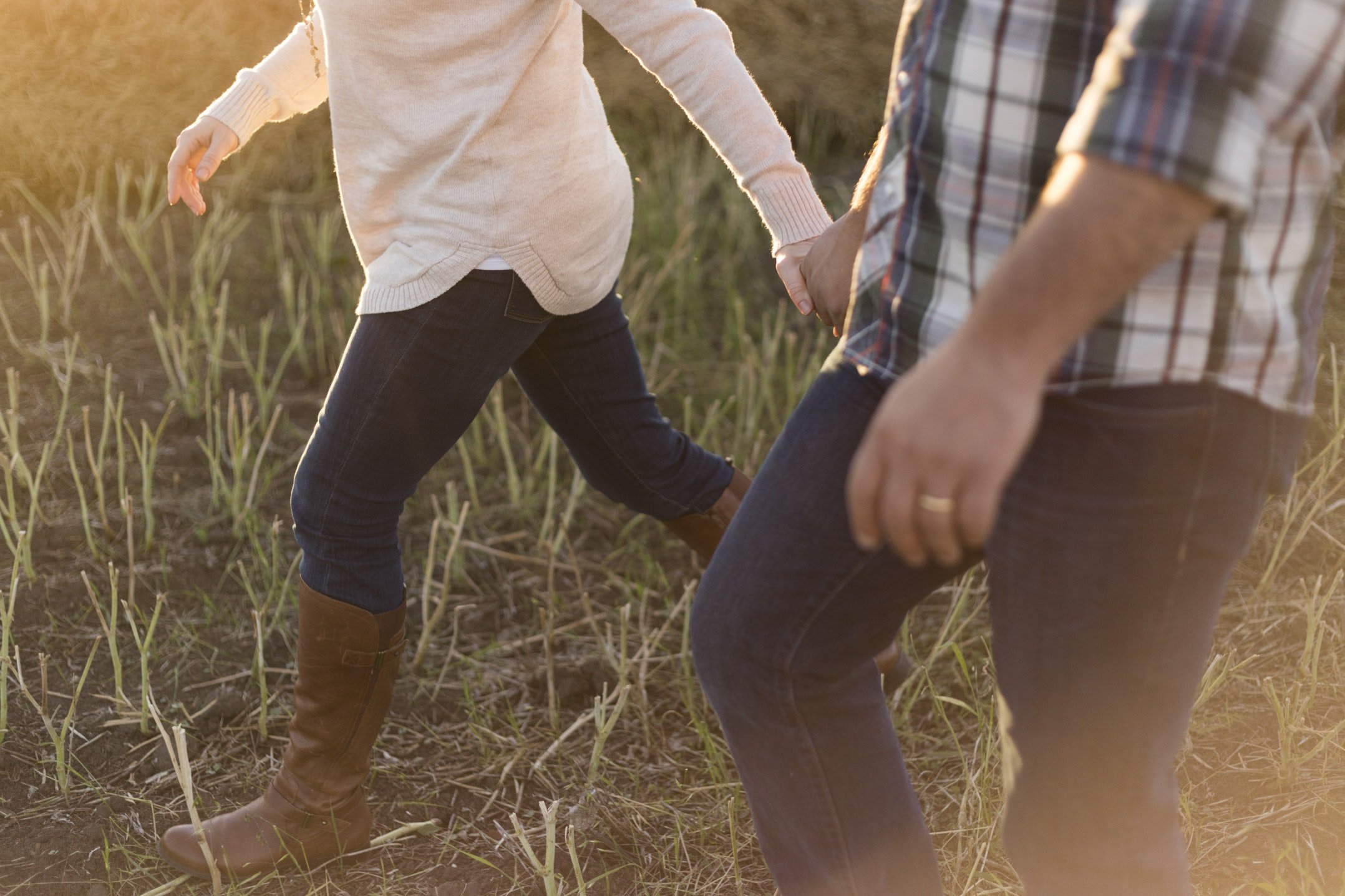 Homem e mulher andam de mãos dadas em um campo.
