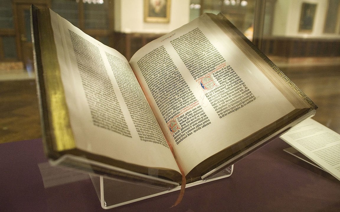 Exemplar da primeira bíblia impressa, a Bíblia de Gutenberg. Exposta em um suporte plástico, aberta na metade.