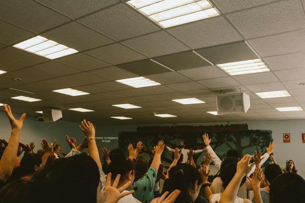 Pessoas com as mãos erguidas frente a pregador em ambiente religioso