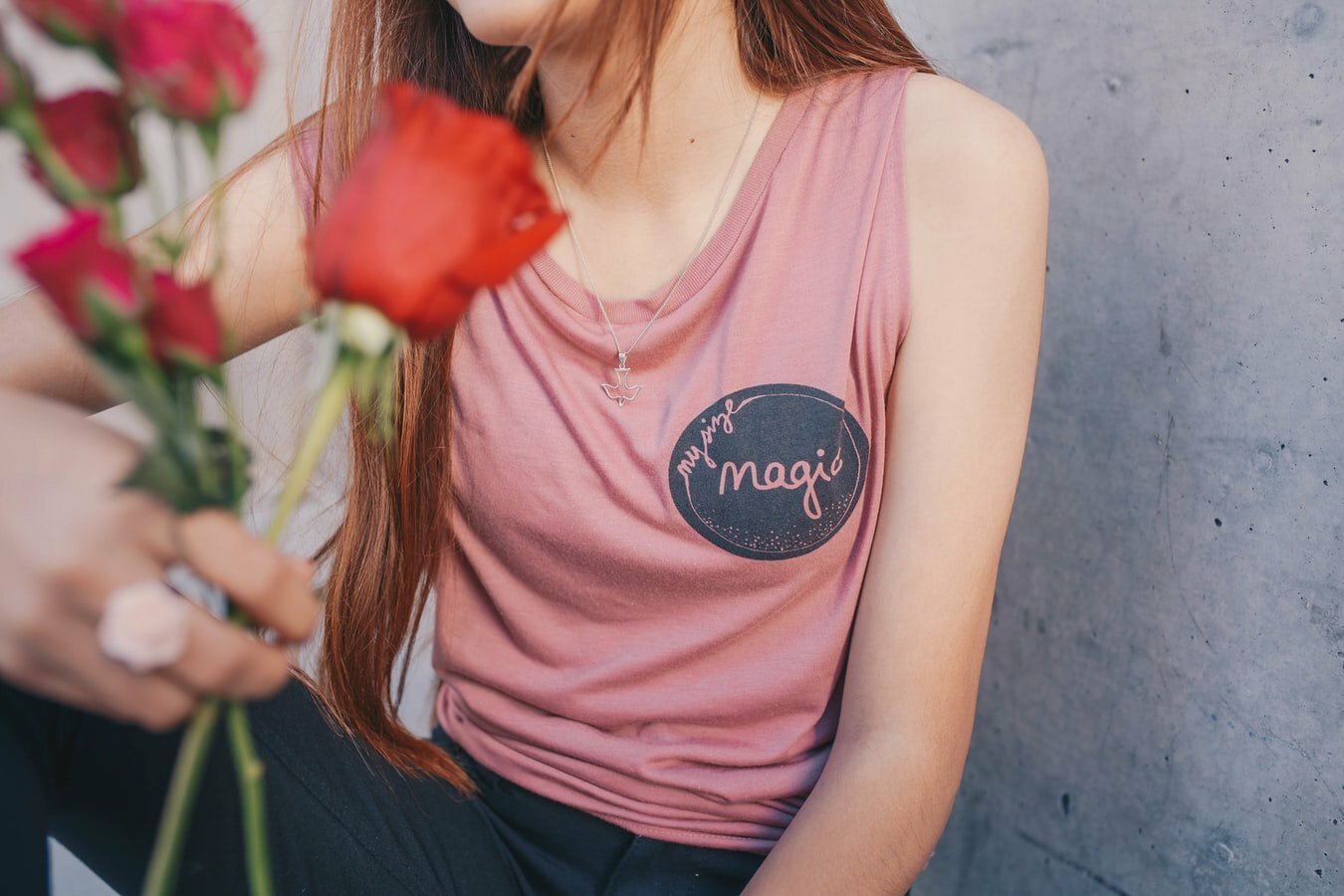Mulher segurando rosas, vestindo uma camiseta rosa sem mangas. Seu rosto não aparece na foto.