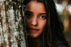 Mulher com o rosto encostado em um tronco de árvore. Ela está sem maquiagem.