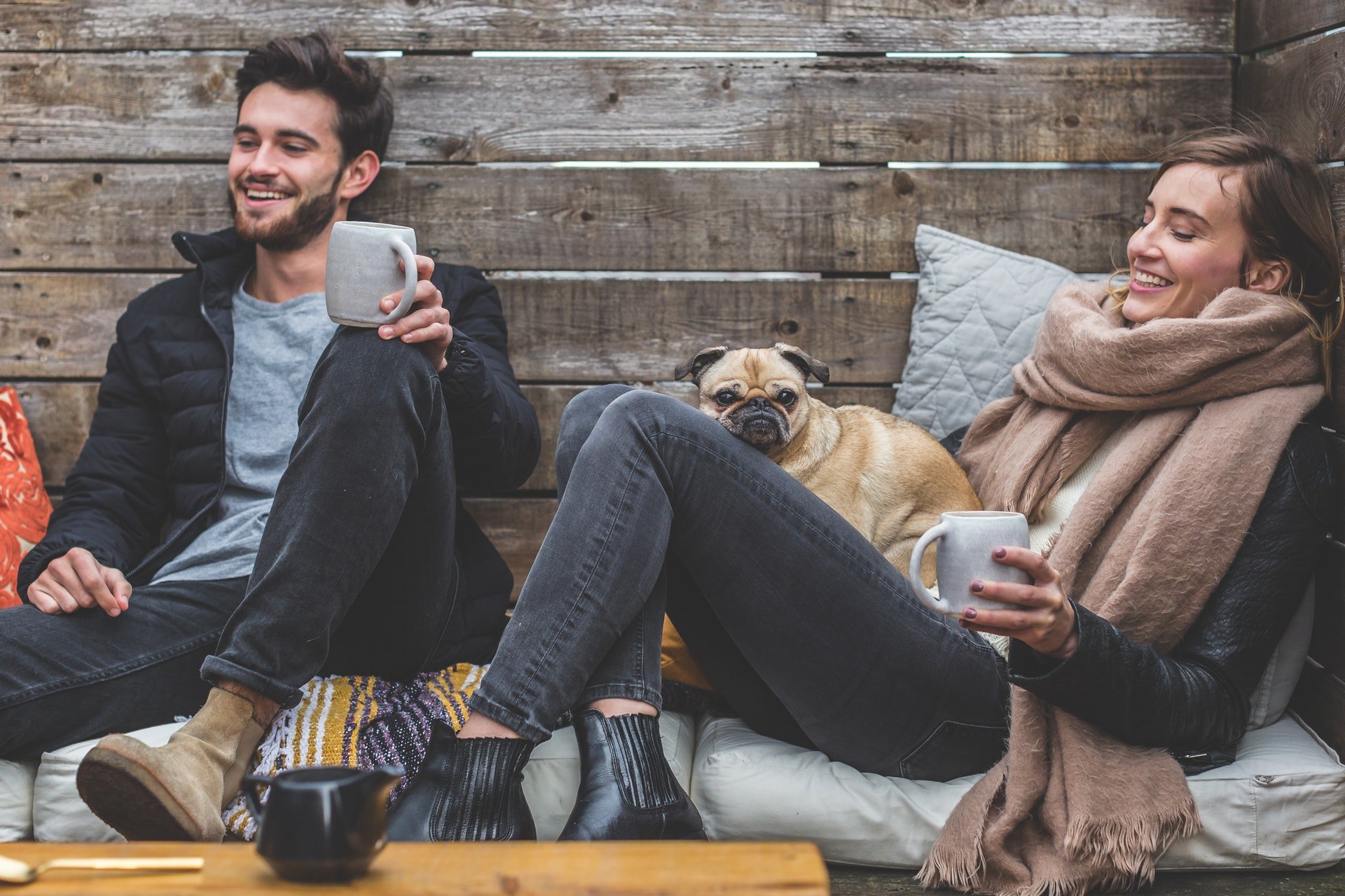 Homem e mulher sentados, sorrindo, com xícaras junto a um cachorro