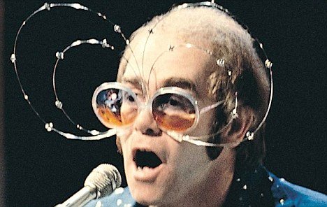 Elton John novo usando óculos com arcos de arames para fora da armação