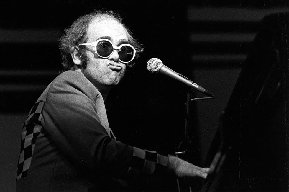 Elton John novo em show, tocando piano e fazendo biquinho para a plateia