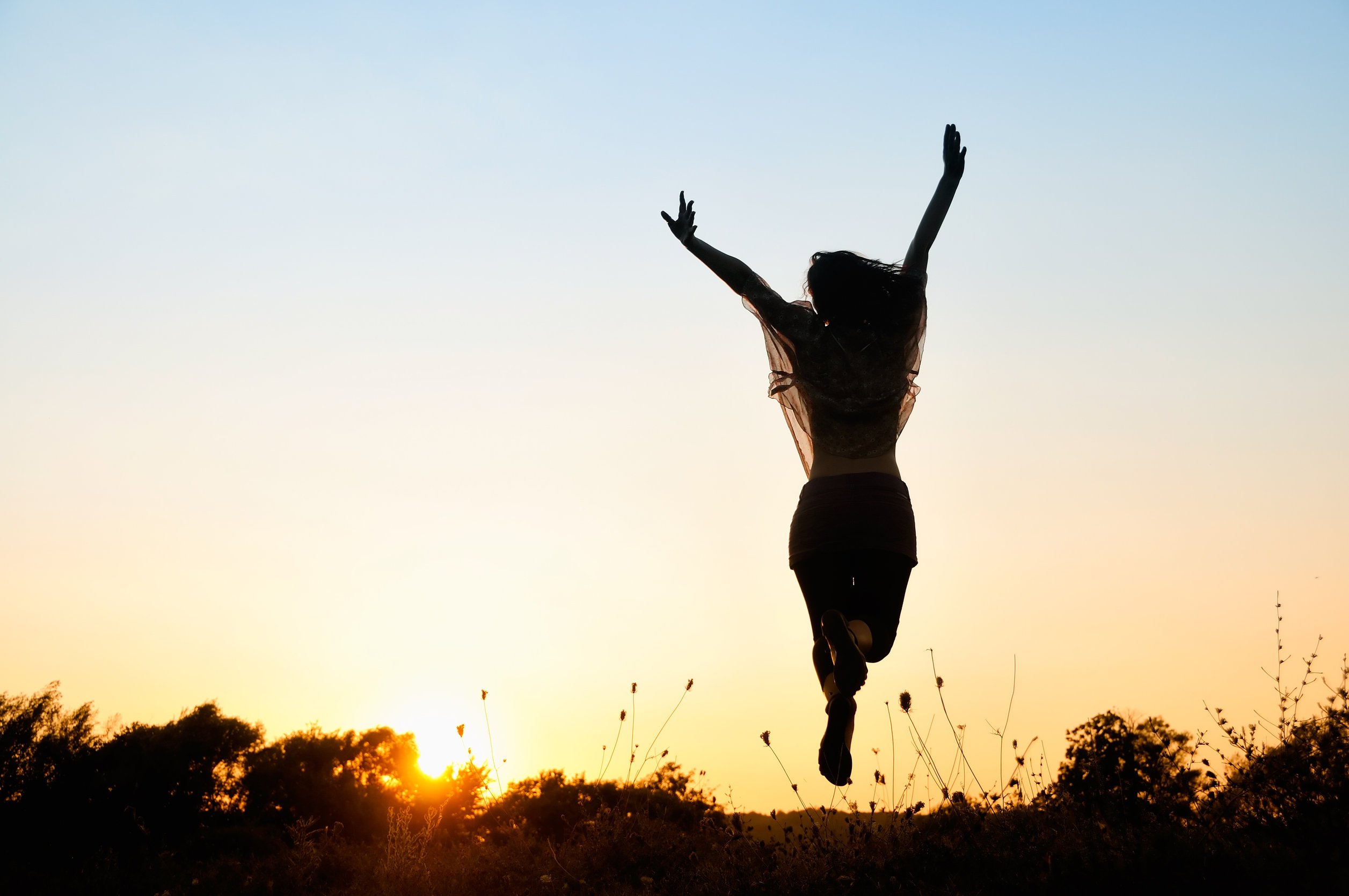 Silhueta de mulher pulando alegremente em paisagem de sol se pondo