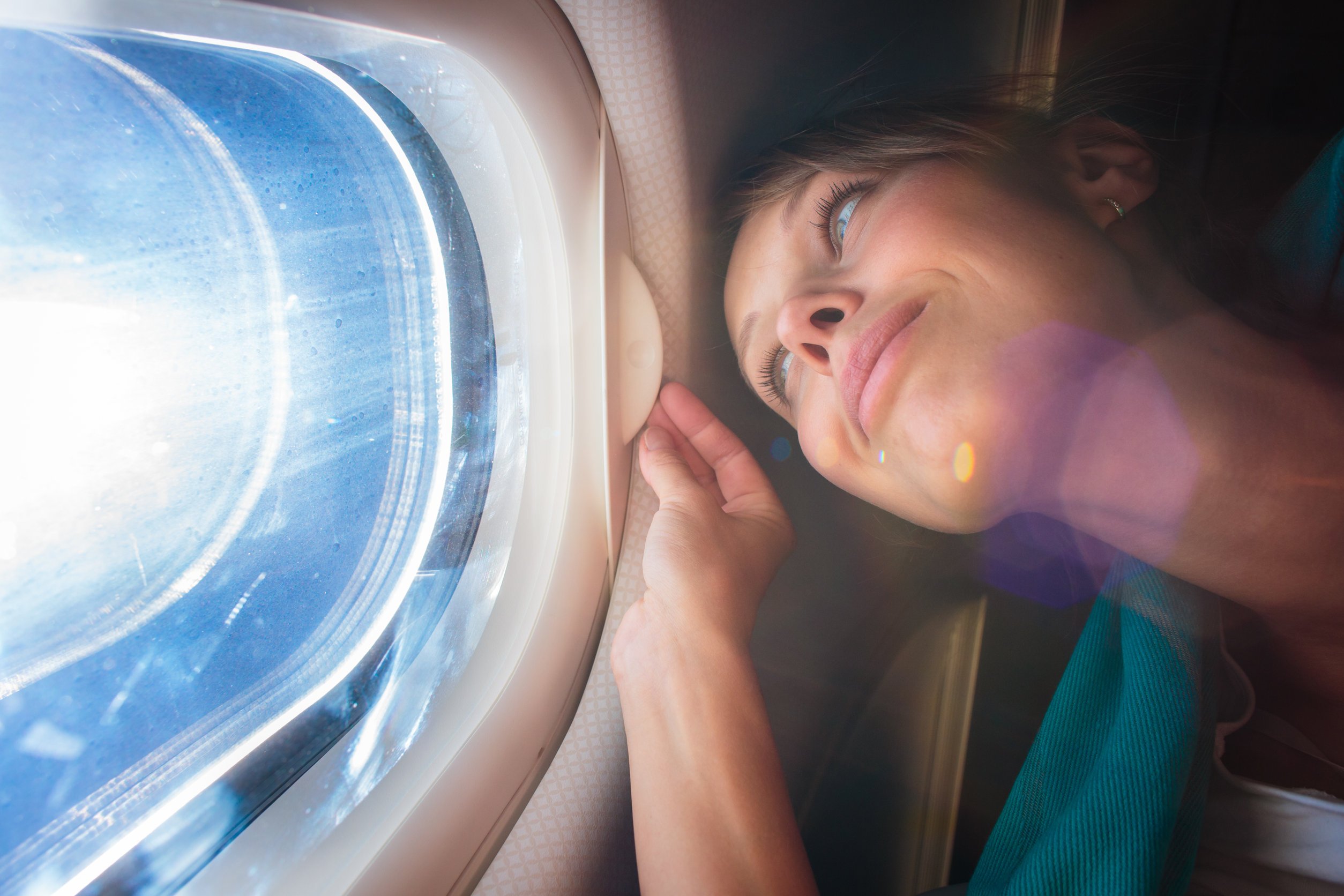 Menina branca de olhos azuis admirando a paisagem de uma janela de avião