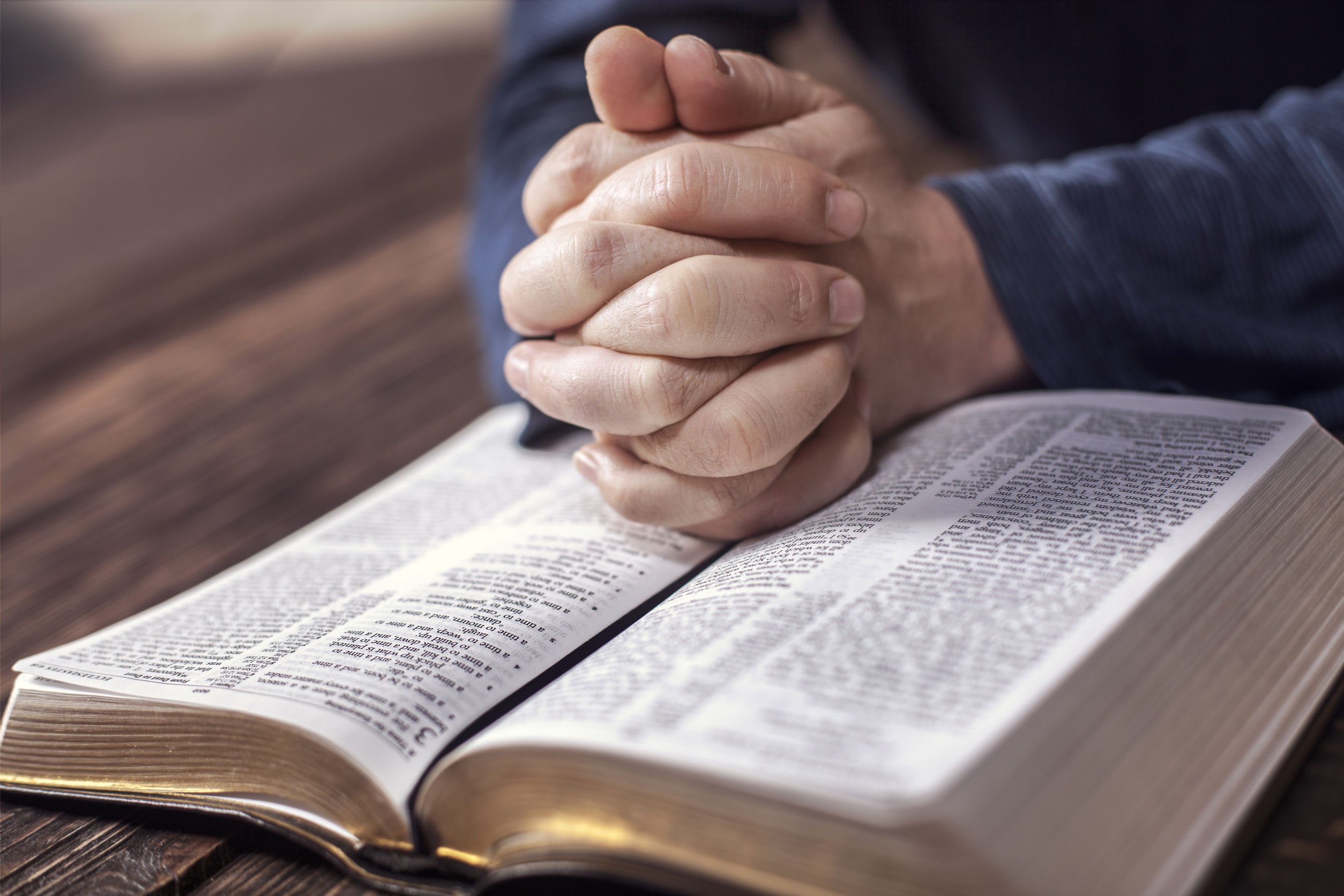 Mãos juntas rezando em cima da bíblia.