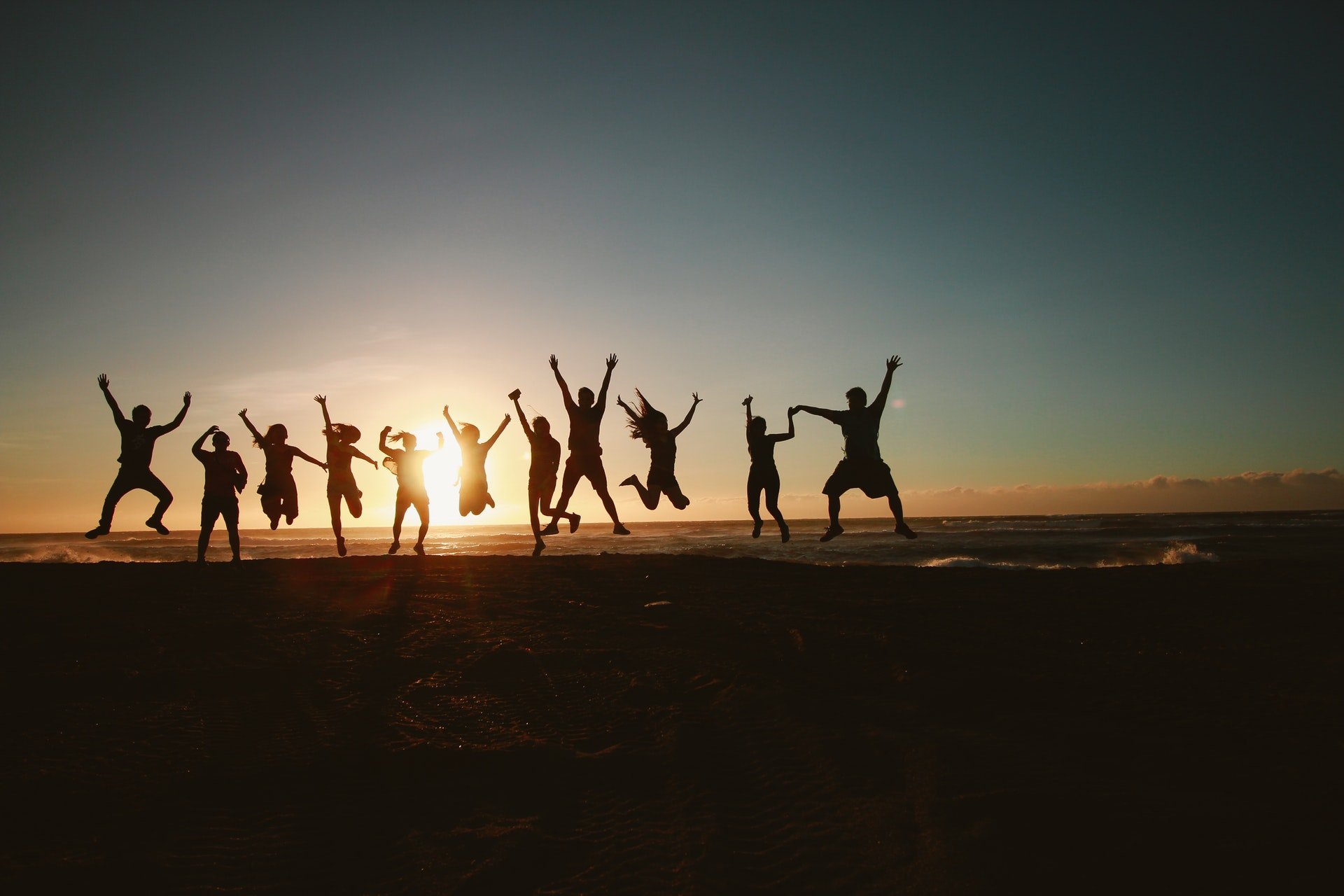 Silhueta de um grupo de amigos pulando frente ao pôr do sol