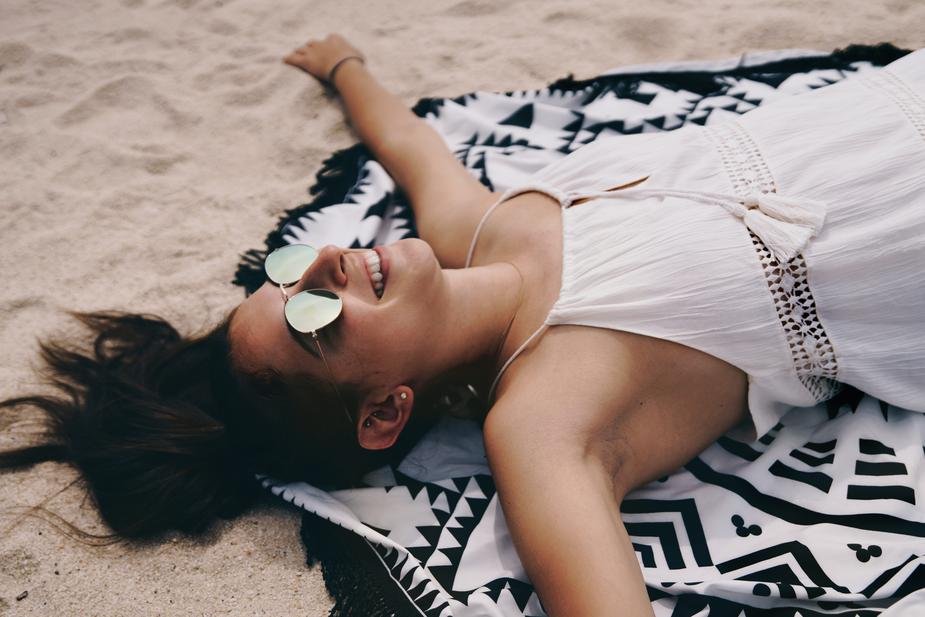 Mulher de óculos escuros deitada na areia, sorrindo