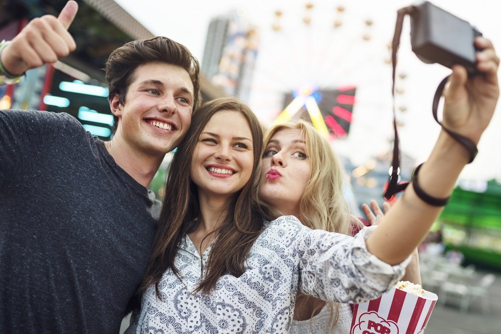 Três amigos tirando selfie num parque de diversões