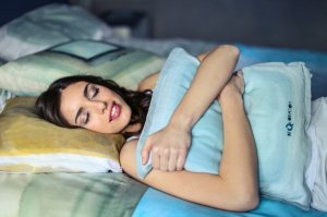 Mulher dormindo na cama abraçada com um travesseiro.