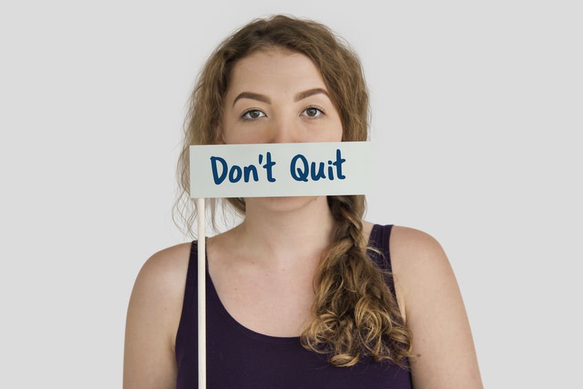 Mulher segurando placa 'Don't Quit' ('não desista', em inglês) em frente à boca