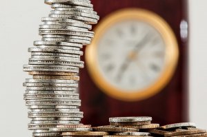 Moedas empilhadas na frente de um relógio desfocado.